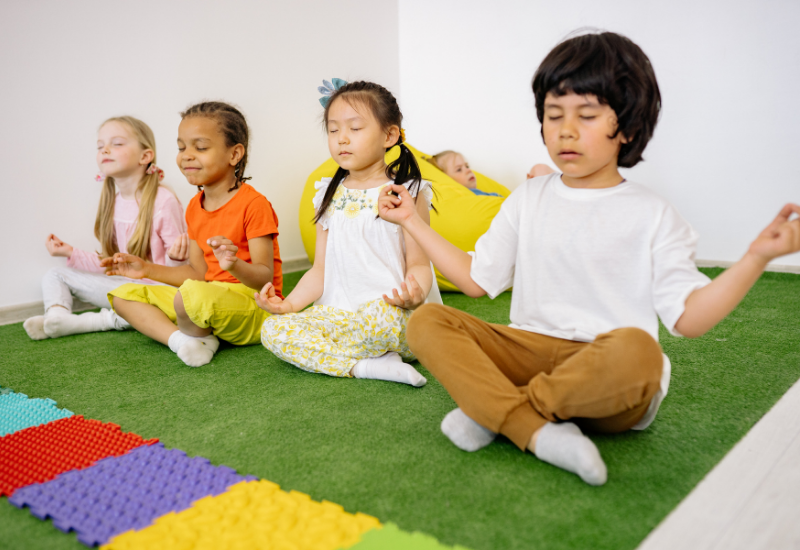 Children meditating on a green mat with colorful blocks around them