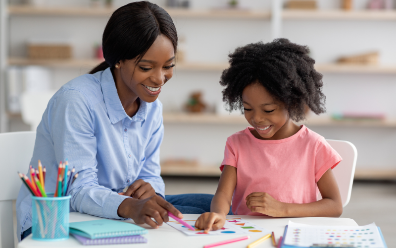 Woman and child sitting at a table with coloring supplies, smiling.